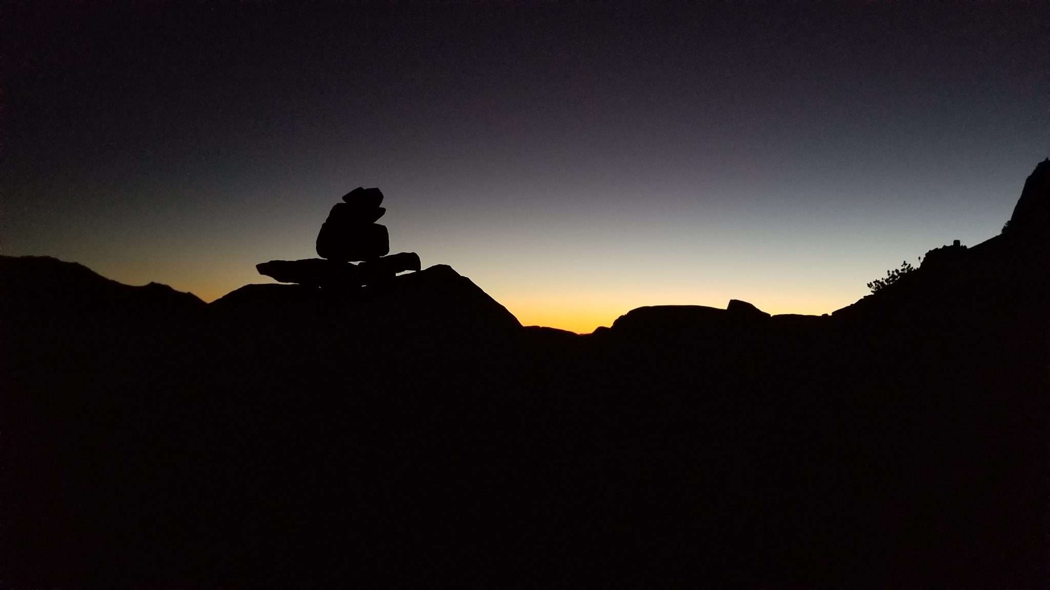 A rock cairn stacked in front of an evening sunset.