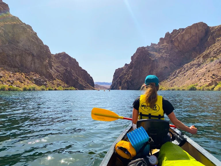Riding in a kayak on the Black Canyon river looking over the shoulder of one Cairn adventure participant and she is paddling.