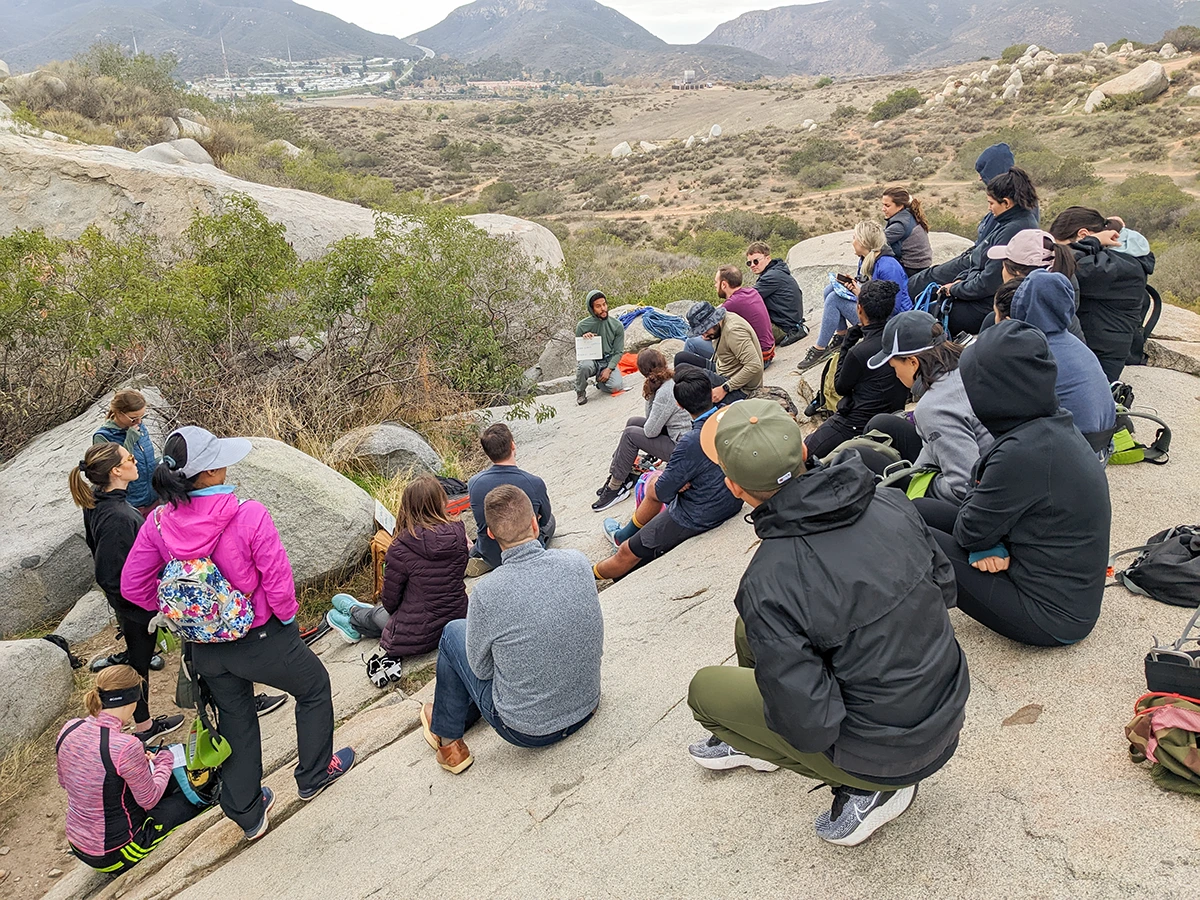 Over 20 Cairn adventure participants seated on rocks listening to a Cairn guide leader discussion on team dynamics.