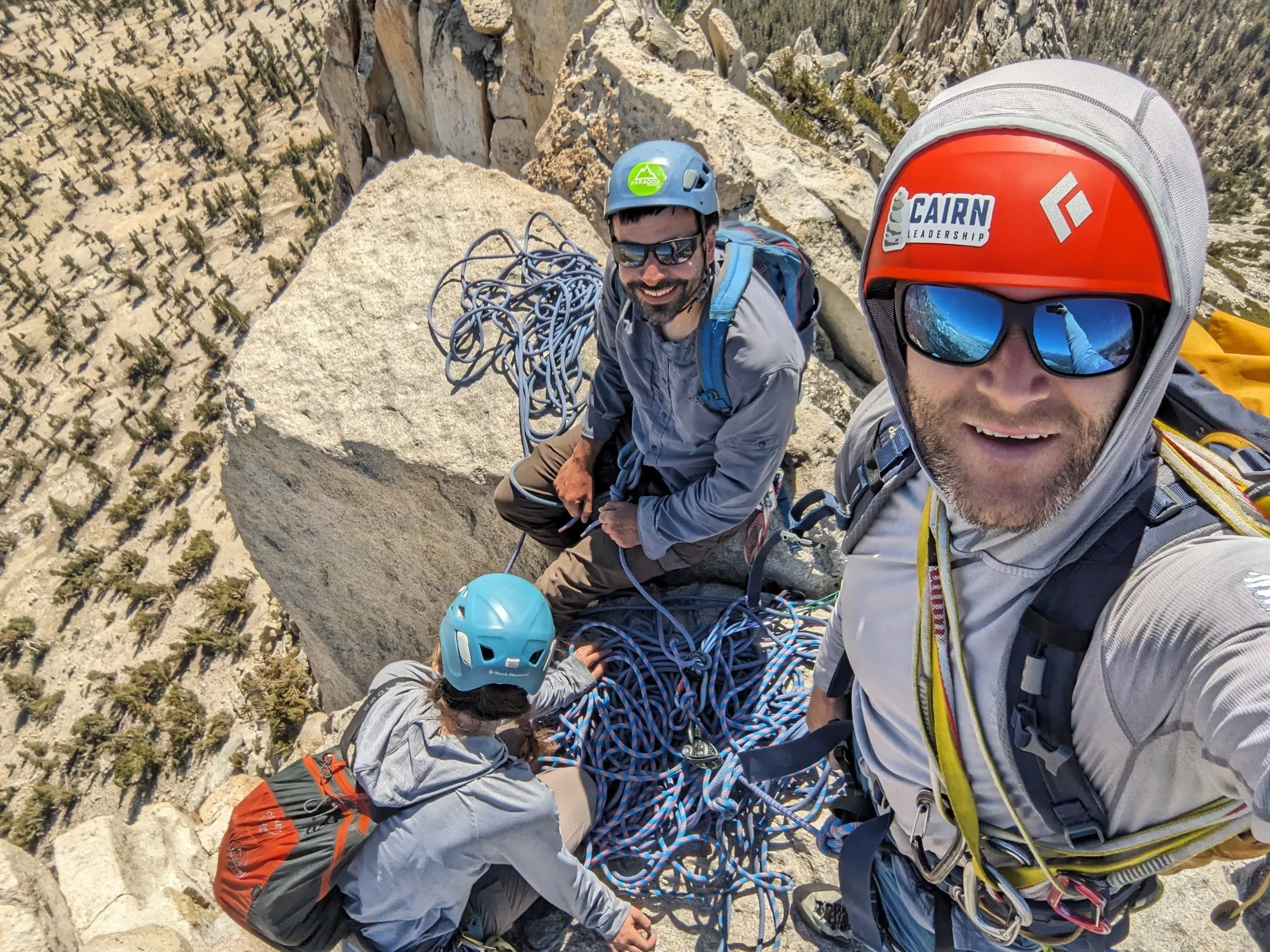Three rock climbers on a cliff top taking a selfie.