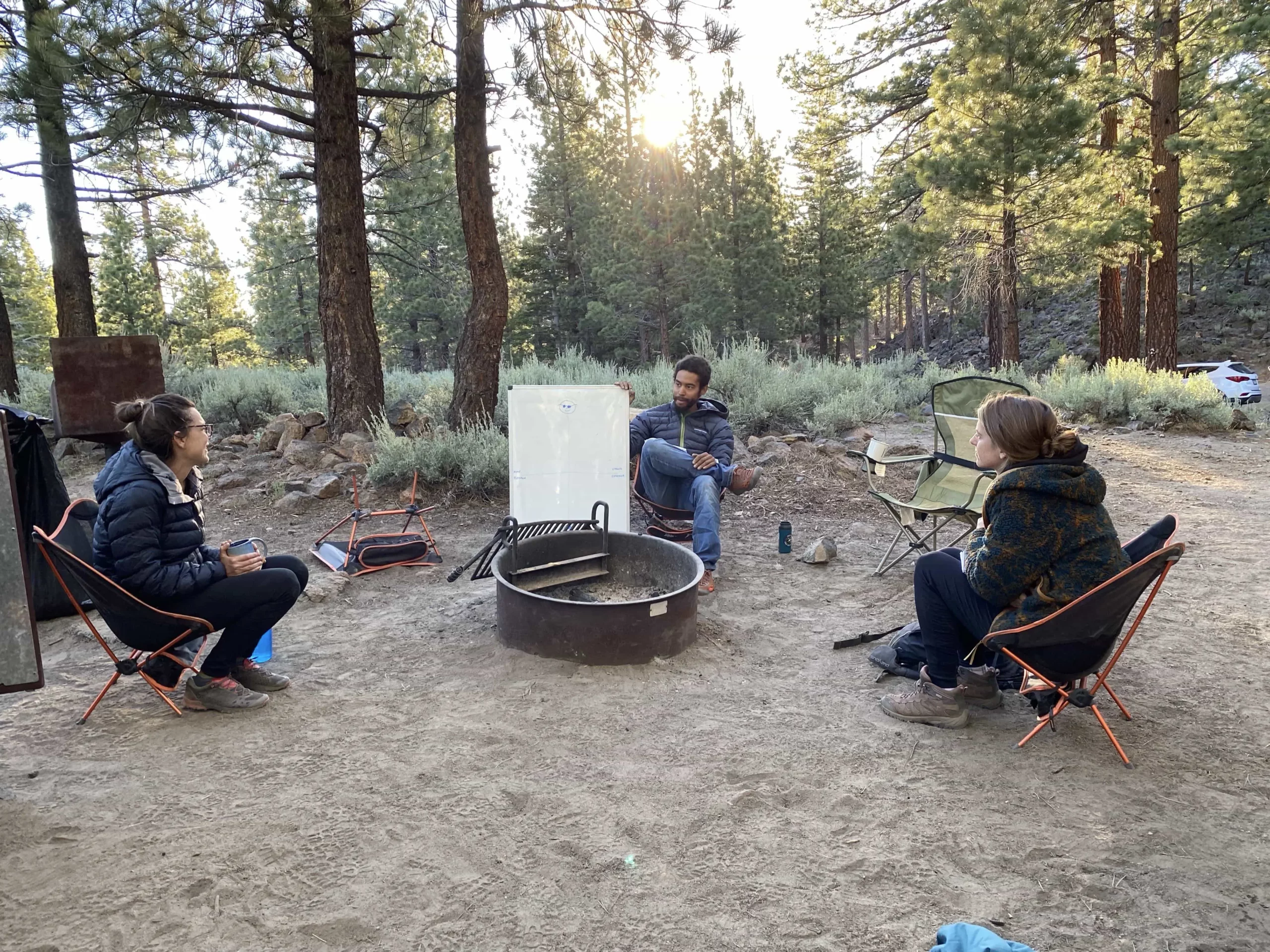 Guide around a campfire ring with two clients discussing how to prevent burnout on a whiteboard