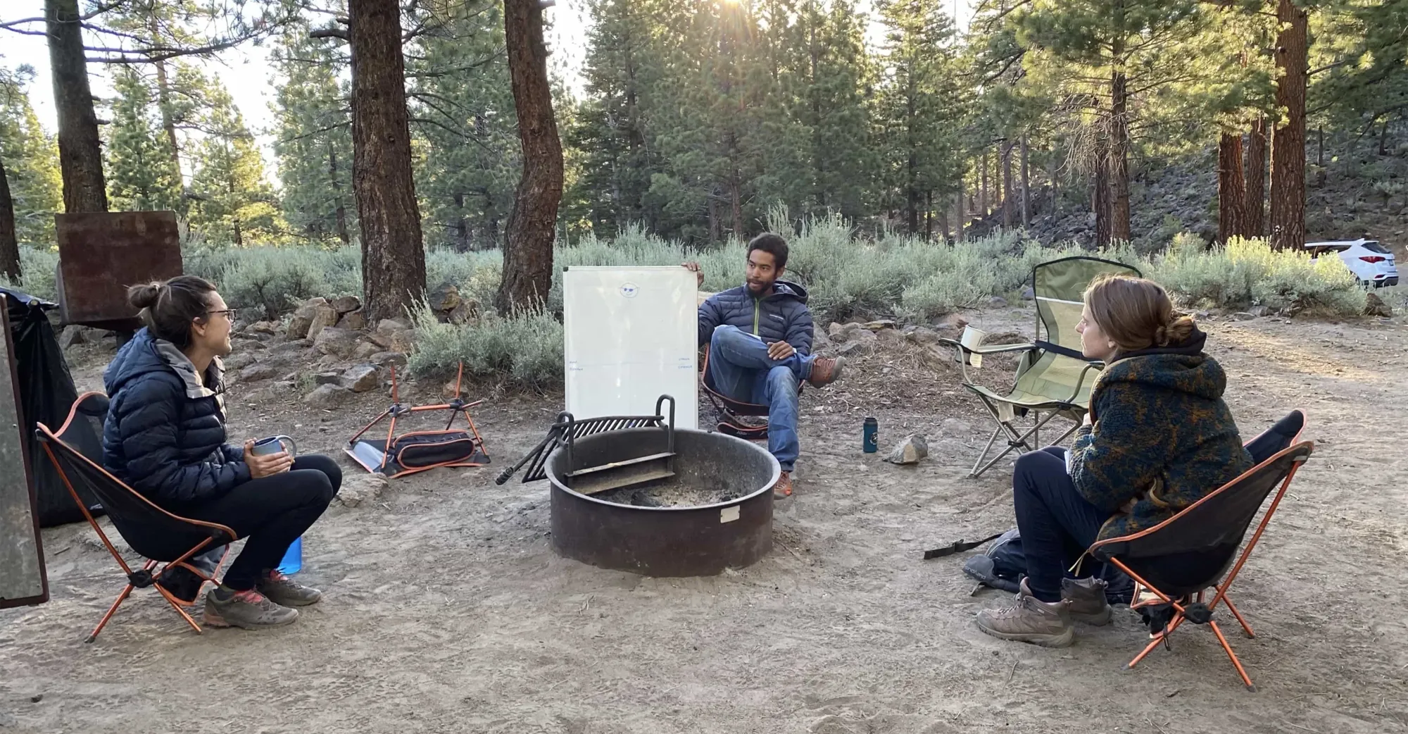 Guide around a campfire ring with two clients discussing how to prevent burnout on a whiteboard
