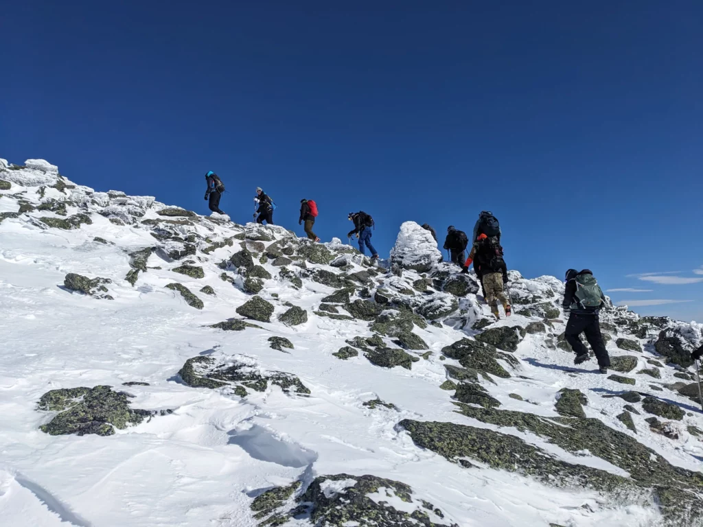 Aline of climbers approach the summit of Mount Washington, surrounded by snow and ice, in a practical example of leading through uncertainty
