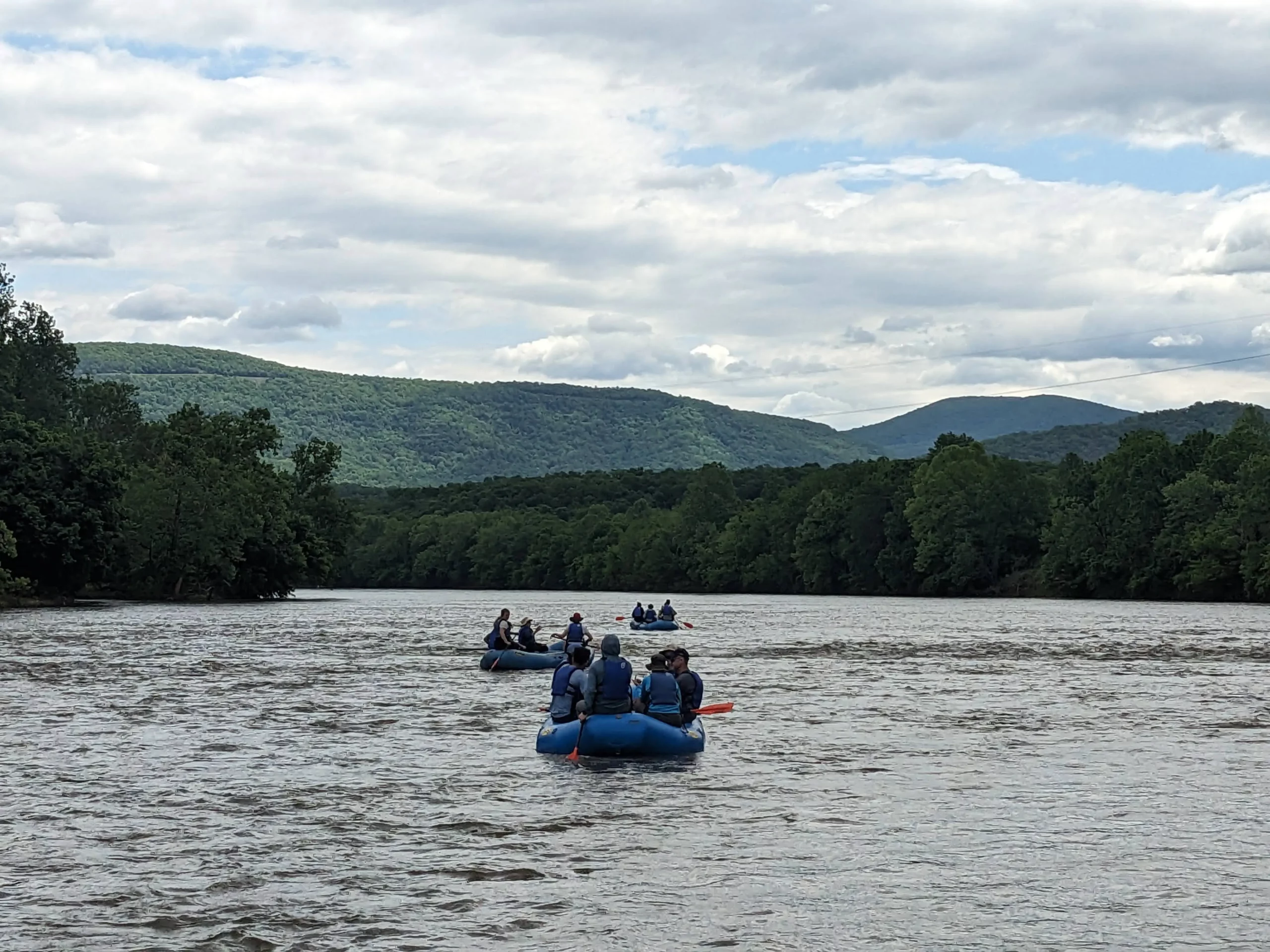 A team of three rafts float down a calm river while the teammates discuss performance management.